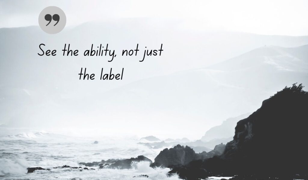 Atmospheric black and white coastal photograph of crashing ocean waves against rugged cliffs, centered with a dark gray quotation icon framing empowering quotes for autism awareness day: "See the ability, not just the label".