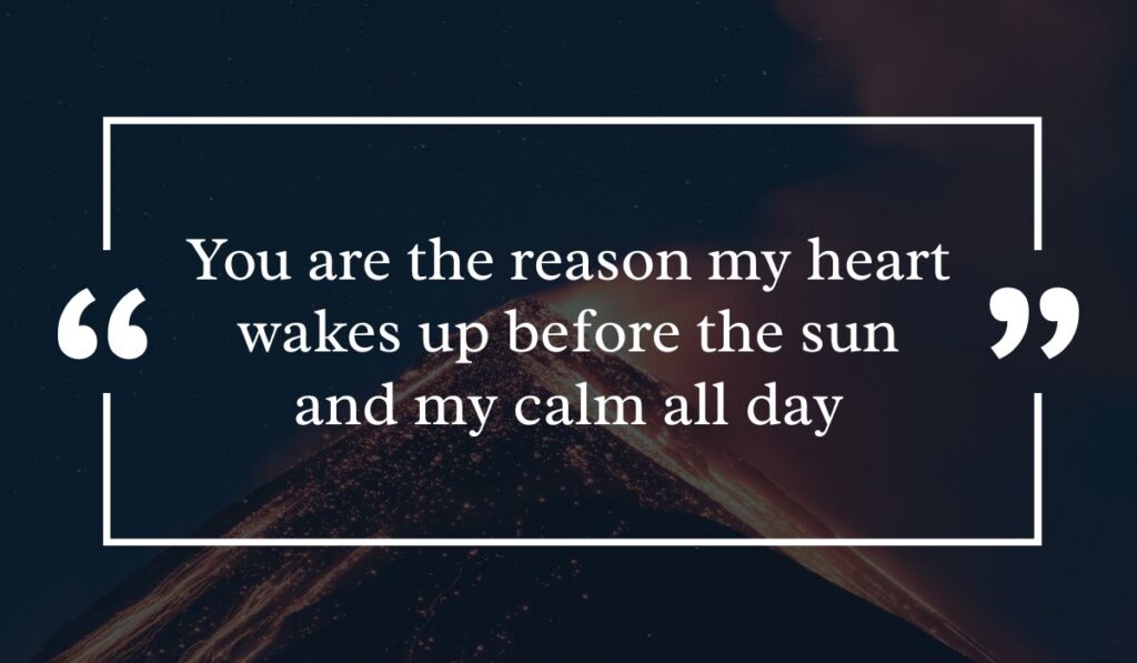 Dramatic dark night sky background featuring a lit volcanic peak at night, centered with a white quotation box highlighting heartfelt best morning messages for him: "You are the reason my heart wakes up before the sun and my calm all day".
