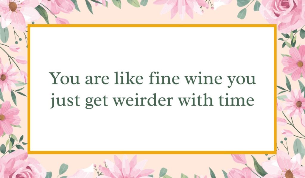Bright white card enclosed by an elegant border of pink watercolor roses and green leaves with a thin gold inner frame, displaying witty birthday wishes for a guy funny: "You are like fine wine you just get weirder with time".