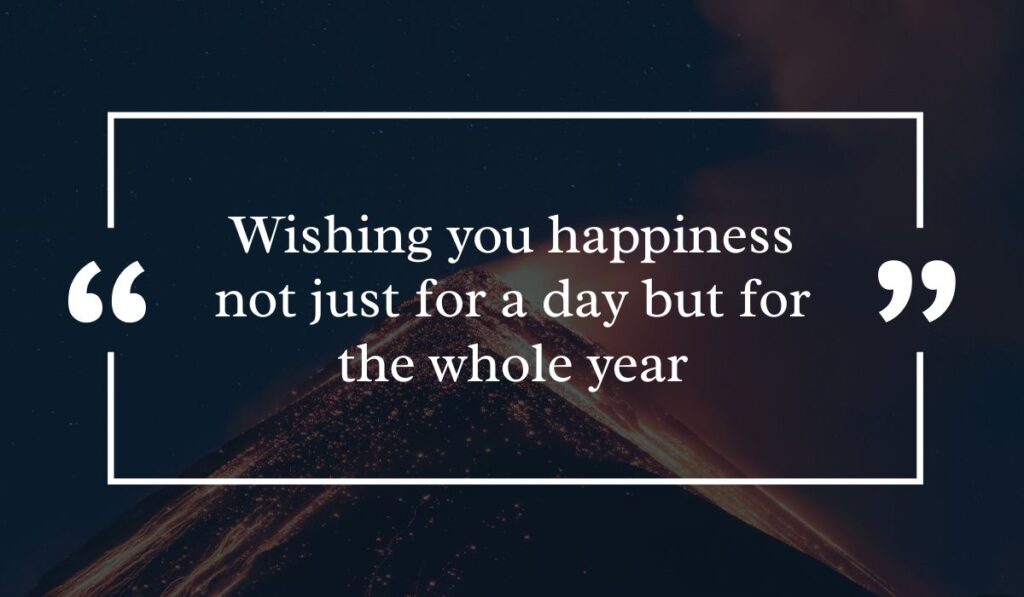 Dramatic dark night sky background featuring a lit volcanic peak at night, centered with a white quotation box highlighting inspiring birthday wishes for belated birthday: "Wishing you happiness not just for a day but for the whole year".