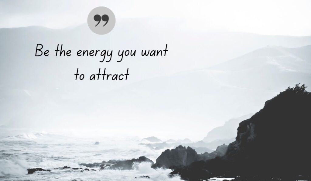Atmospheric black and white coastal photograph of crashing ocean waves against rugged cliffs, centered with a dark gray quotation icon framing encouraging Facebook quotes for cover photo: "Be the energy you want to attract".