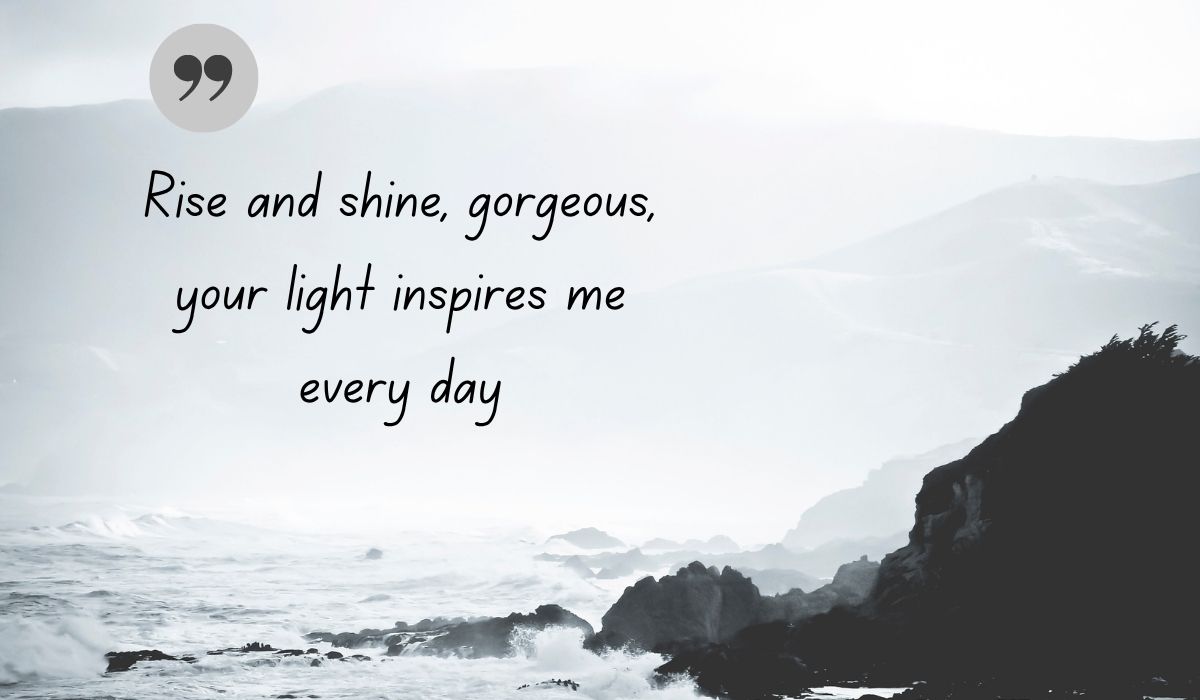 Atmospheric black and white coastal image of crashing ocean waves against rocky cliffs, centered with a thin, delicate gray circle and a dark green quotation icon framing the handwritten literary text, "Rise and shine, gorgeous, your light inspires me every day".